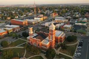 Aerial view of a small-town courthouse with a clock tower, surrounded by historic buildings, streets, and trees.