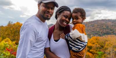 Mother holding son with father next to them in front of fall mountain backdrop