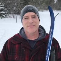 a person poses for the camera in a winter scene holding cross country skis