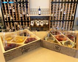 This picture is from Neighbor Lady Vino winery and shows two sets of wine flights ready to be enjoyed. In the background you can see a full wall of the Neighbor Lady Vino wine bottles on display.