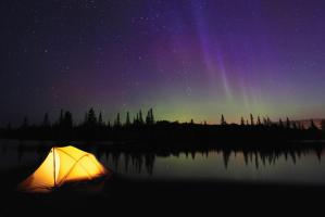 Lit tent next to lake with northern lights in the sky