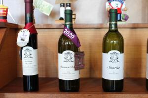 Three bottles of unopened wines sit along a wooden shelf. Two of the bottles of wine display awards around the neck of the bottle.