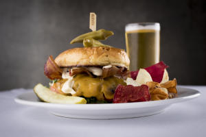 Close-up shot of a cheeseburger and chips with a glass of beer in the background