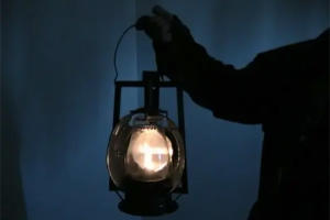 A man is holding an old gas lantern in the dark.