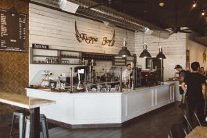 Interior of a local coffee house with a couple customers and a barista preparing drinks behind the counter