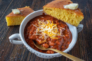 Bowl of chili topped with shredded cheese and a side of cornbread