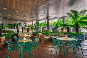 Inside of Hyatt Hotel Cambridge restaurant area - small round tables with green chairs around them with a soft LED light in the. There is also green foliage around the venue to make it feel like the outside is inside middle