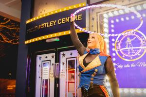 A circus performer prepares to entertain with some spectacular hula hoop tricks, outside The Philip Astley Centre at night