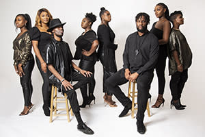 Image shows the men and women of the London Community Gospel Choir, mostly standing with a couple sitting on stools
