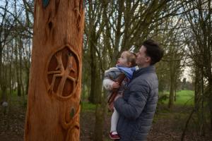 A father lifts his little girl up to show her one of the wood carvings on The Stick Man Trail at the National Memorial Arboretum, Staffordshire