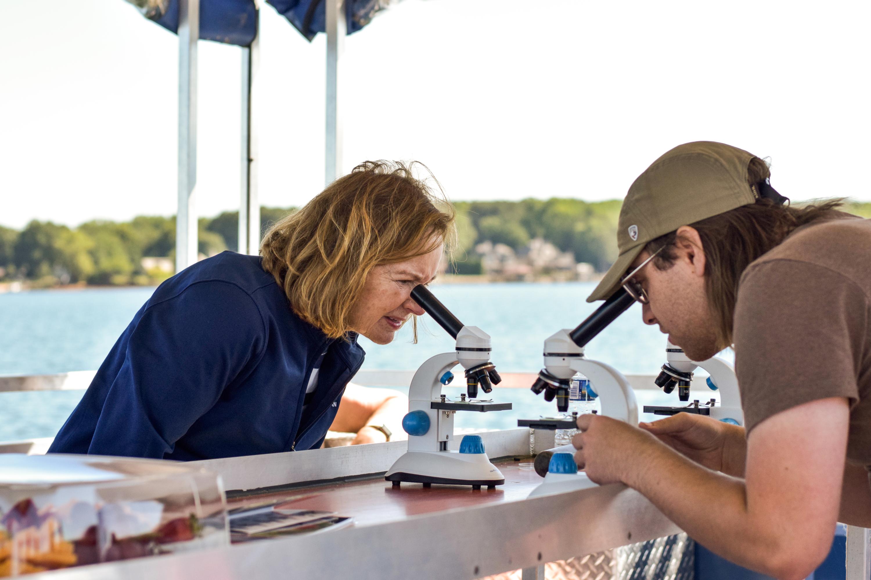 A man and a woman are looking into two microscopes on the Catawba Riverkeeper Floating Classroom in Lake Norman.