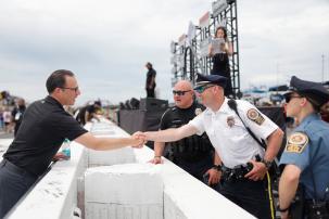The Governor of Pennsylvania, Josh Shapiro, leaning over a half wall and shaking a cops hand