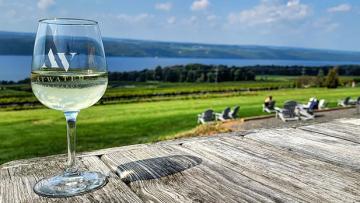A glass on wine sitting on a wooden boardwalk with views of Seneca Lake in the background