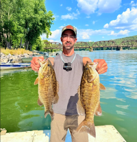 Vincent Stuter of Anglers Anchor standing on a dock by the river holding a double catch = one fish in each hand.