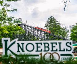 Picture of a Knoebels 100 sign with the Phoenix Roller Coaster in the background.