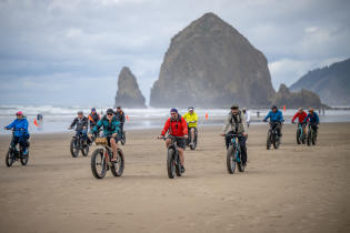 Group of riders on fat tire bikes riding on beach in front of Haystack Rock