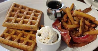 Plate with waffles, bacon, fries, and butter and syrup.