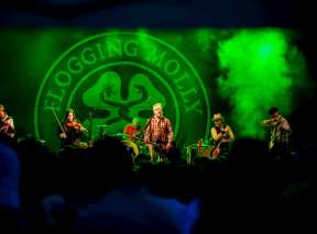 Flogging Molly on stage with green lights and smoke at Wichita Riverfest with massive crowd