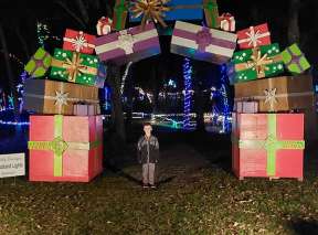 A boy poses under an arch of Christmas presents at A Country Christmas at Fulton Valley Farms