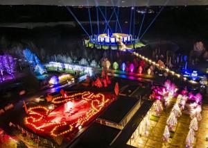 Image shows a night time scene at the National Memorial Arboretum, with colourful lighting on and around the memorials and beams of light shining into the sky around the Armed Forces Memorial