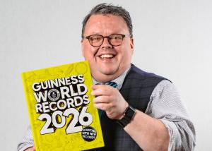 Image shows Guinness World Records editor-in-chief Craig Glenday, holding the 2026 edition and smiling at the camera