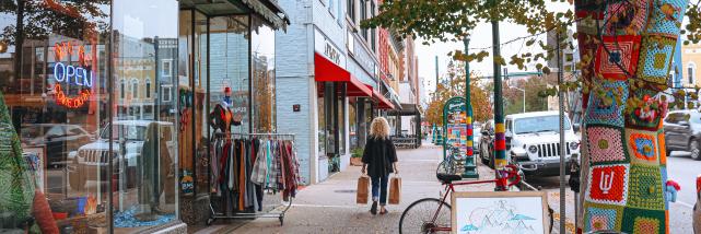 A woman walking with shopping bags toward Goods for Cooks on The Square