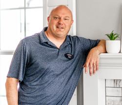 Allen Woody, standing at a fireplace with his elbow propped on the mantle.