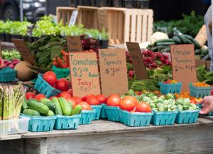 Homegrown Produce on display with hand written signs listing for sale price of vegetables at a farmers market.