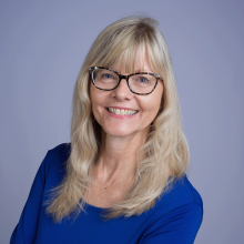 mary headshot - caucasian woman with long blond hair and blue eyes wearing a long sleeve royal blue shirt and glasses