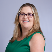 Braley headshot - caucasian women with light brown hair and green eyes wearing glasses and a green dress