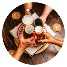 Guests holding craft beers cheersing at rustic table