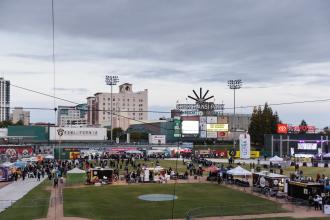 Photo shows taco trucks lined up on field of Chukchansi Park in Fresno as guests stand in line for food