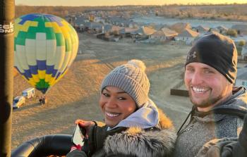 smiling couple in a hot balloon - ground in the background