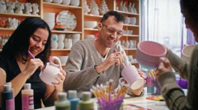 Two people sitting at a table painting ceramics.