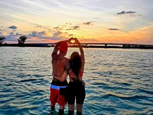 Couple standing in water at sunset, creating "heart hands"