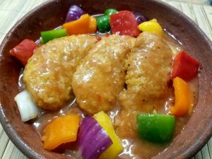 Breaded and fried chicken patties surrounded by chopped pieces of purple onion, and green, red, and yellow peppers.