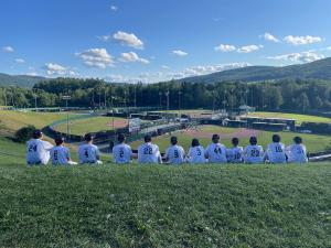 A youth baseball team sitting on a hill overlooking baseball fields