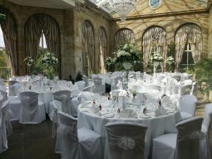 The Orangery at Weston Park, Staffordshire, all set up for a wedding reception, with beautiful white tablecloths and furnishings, and sunlight streaming in through the large windows