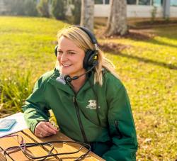 Christina Cooper, executive director of Global Wildlife Center, sits outdoors at a wooden table wearing a headset microphone, smiling during an interview.
