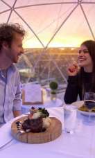 A couple dining in a rooftop igloo at sunset.