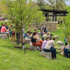 Picture of people sitting on rocks at Hufnagle in Downtown Lewisburg on a sunny spring day with trees in bloom.