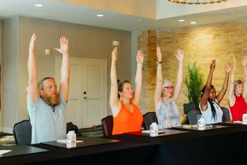 Group of adults sitting at conference table doing yoga stretch break