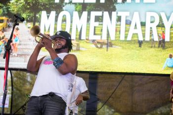 Man playing a trumpet on stage with a sign that says "Momentary" in the background