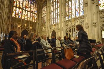 A group people sitting down listening to a tour guide in King's College Chapel