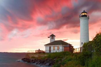 Tibbitts Pointe Lighthouse - Cape Vincent A white lighthouse with the backdrop of a orange and purple sunset