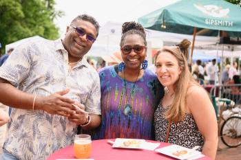 Three people stand at a table smiling at the Wine & Food Festival.