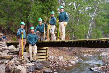 Great Lakes Climate Corp workers standing on and alongside a bridge that they built in summer 2023