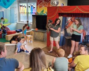 Presentation in the stage room at the Lewisburg Children's Museum with people watching the show and kids playing in the background.