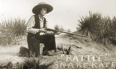 Rattlesnake Kate kneeling on the ground with her rifle in hand.