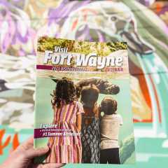 2023 Visitors Guide magazine held in front of a mural